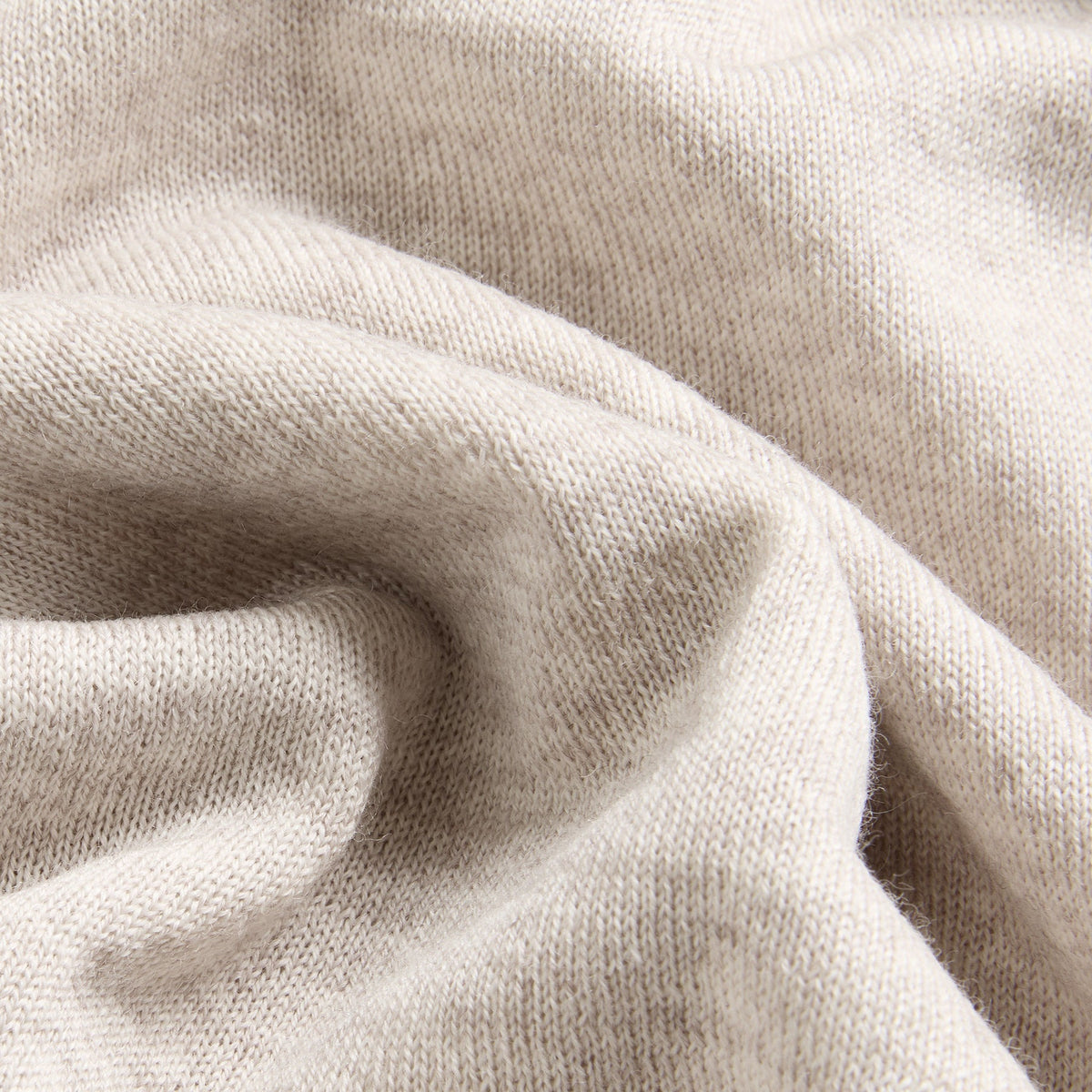 A close-up of draped knit fabric in a light warm off-white or cream tone, showing the texture and folds of the material. Oliver Sweeney knitwear available at Sakks Menswear in Southampton.