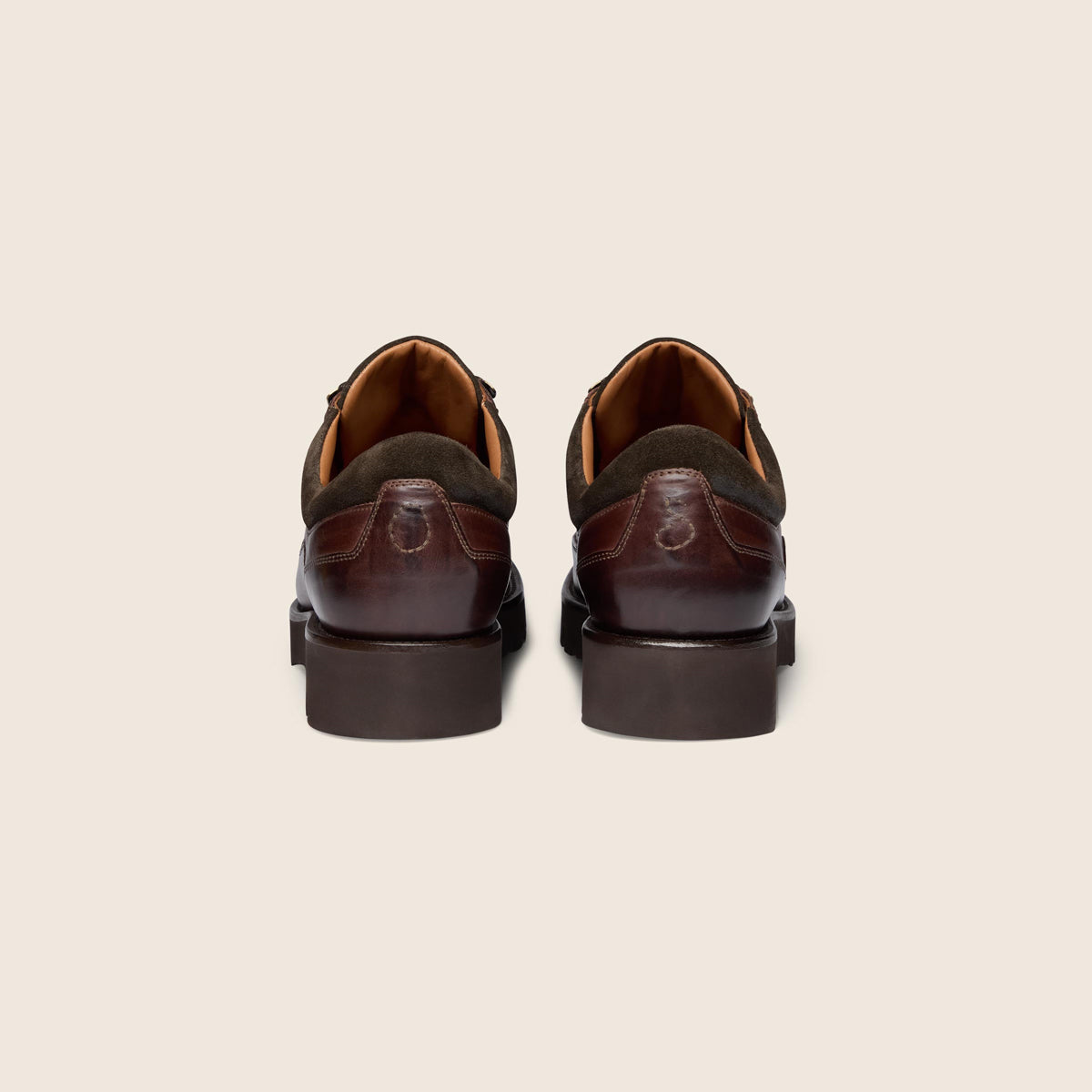 A pair of men's dark brown leather and suede oxford shoes shown from the back, positioned side-by-side against a solid light beige background. Oliver Sweeney Boots available at Sakks Menswear in Southampton.