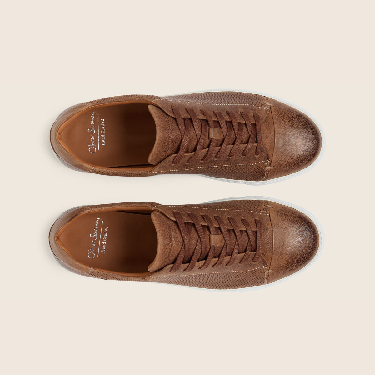 A pair of brown leather low-top sneakers shown from a top-down view on a light beige background. The shoes feature matching brown laces, a rounded toe, and the brand name 'Oliver Souchay Paris Couture' printed in gold on the insole. Oliver Sweeney Trainers available at Sakks Menswear in Southampton.