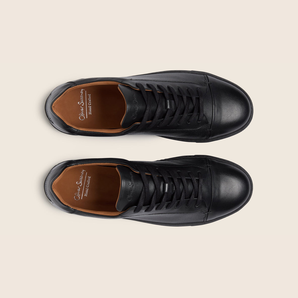 A pair of black leather low-top lace-up shoes shown from a top-down view on a light beige background. The shoes feature a smooth black leather upper, black laces, and a contrasting tan-brown leather interior with 'Oliver Sweeney' branding visible. Oliver Sweeney Trainers available at Sakks Menswear in Southampton.