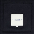 A close-up of a dark navy or black textured fabric with a centered white square label reading 'PROFUOMO' in blue text.  Profuomo Coat available at Sakks Menswear in Southampton.