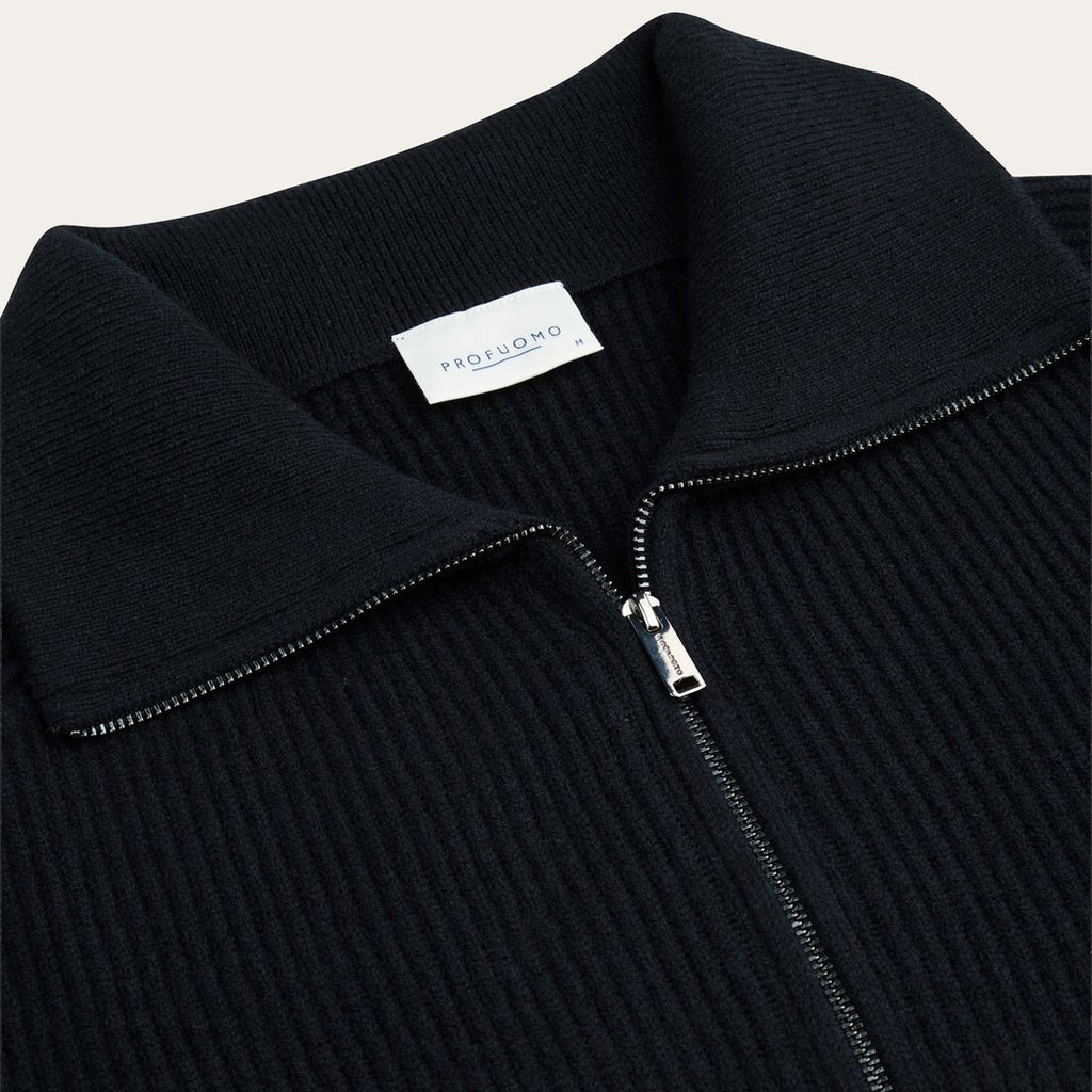 Close-up of a ribbed knit zip-up sweater collar in black, with a white neck label reading PROFUOMO and a silver zipper pull. Profuomo Knitwear available at Sakks Menswear in Southampton.