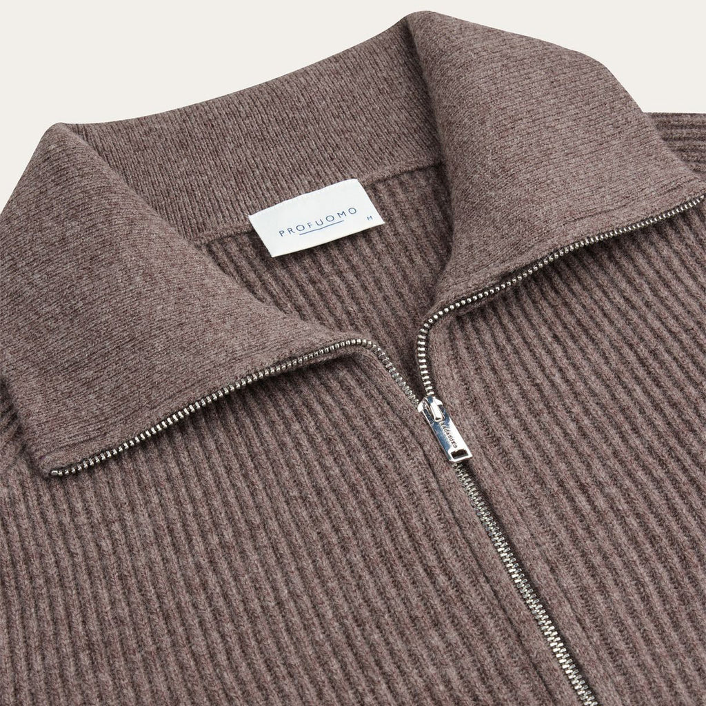 Close-up of a ribbed knit zip-up sweater in a muted taupe-brown color, featuring a collar and a silver zipper. A white neck label reads 'PROFUOMO'. Profuomo Knitwear available at Sakks Menswear in Southampton.