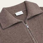 Close-up of a ribbed knit zip-up sweater in a muted taupe-brown color, featuring a collar and a silver zipper. A white neck label reads 'PROFUOMO'. Profuomo Knitwear available at Sakks Menswear in Southampton.