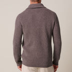 A man viewed from the back wearing a ribbed knit polo-style sweater in a muted taupe-brown color, paired with light beige trousers, against a plain light beige studio background. Profuomo Knitwear available at Sakks Menswear in Southampton.