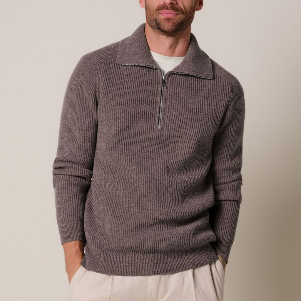 A man wearing a ribbed knit quarter-zip sweater in a muted taupe-brown color, layered over a white t-shirt and paired with light beige trousers, against a plain beige studio background. Profuomo Knitwear available at Sakks Menswear in Southampton.