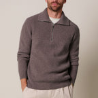 A man wearing a ribbed knit quarter-zip sweater in a muted taupe-brown color, layered over a white t-shirt and paired with light beige trousers, against a plain beige studio background. Profuomo Knitwear available at Sakks Menswear in Southampton.