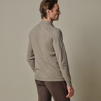 A man wearing a light gray long-sleeve mock neck sweater, shown from a three-quarters back view against a solid warm gray background. Profuomo Polo available at Sakks Menswear in Southampton.