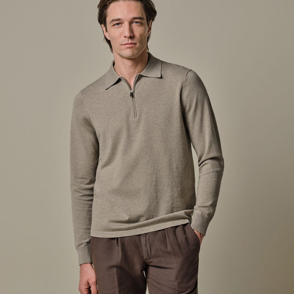 A man wearing a light taupe-gray long-sleeve quarter-zip polo sweater and brown trousers, standing against a solid neutral beige background. Profuomo Polo available at Sakks Menswear in Southampton.