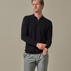 A man wearing a dark navy long-sleeve quarter-zip polo shirt and light gray trousers, standing against a solid beige studio background. Profuomo Polos available at Sakks Menswear in Southampton.