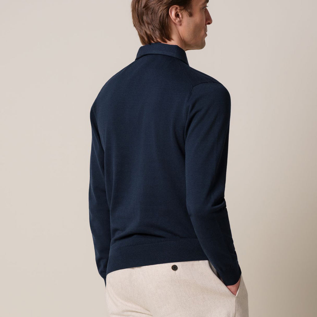 A man shown from the back wearing a dark navy blue knit polo shirt and light beige trousers, photographed against a plain light beige studio background. Profuomo Polos available at Sakks Menswear in Southampton.