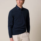 A man wearing a dark navy long-sleeve polo shirt and light beige trousers, standing against a plain beige studio background. Profuomo Polos available at Sakks Menswear in Southampton.