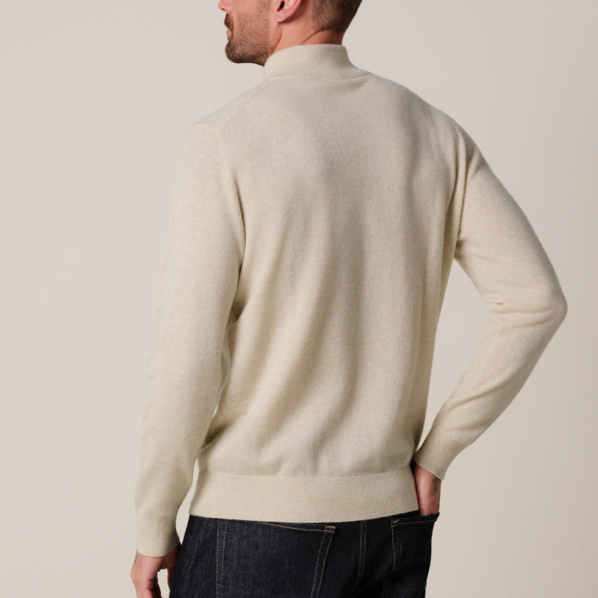 A man wearing a cream-colored knit mock neck sweater, shown from the back against a solid light beige background. Profuomo knitwear available at Sakks Menswear in Southampton.