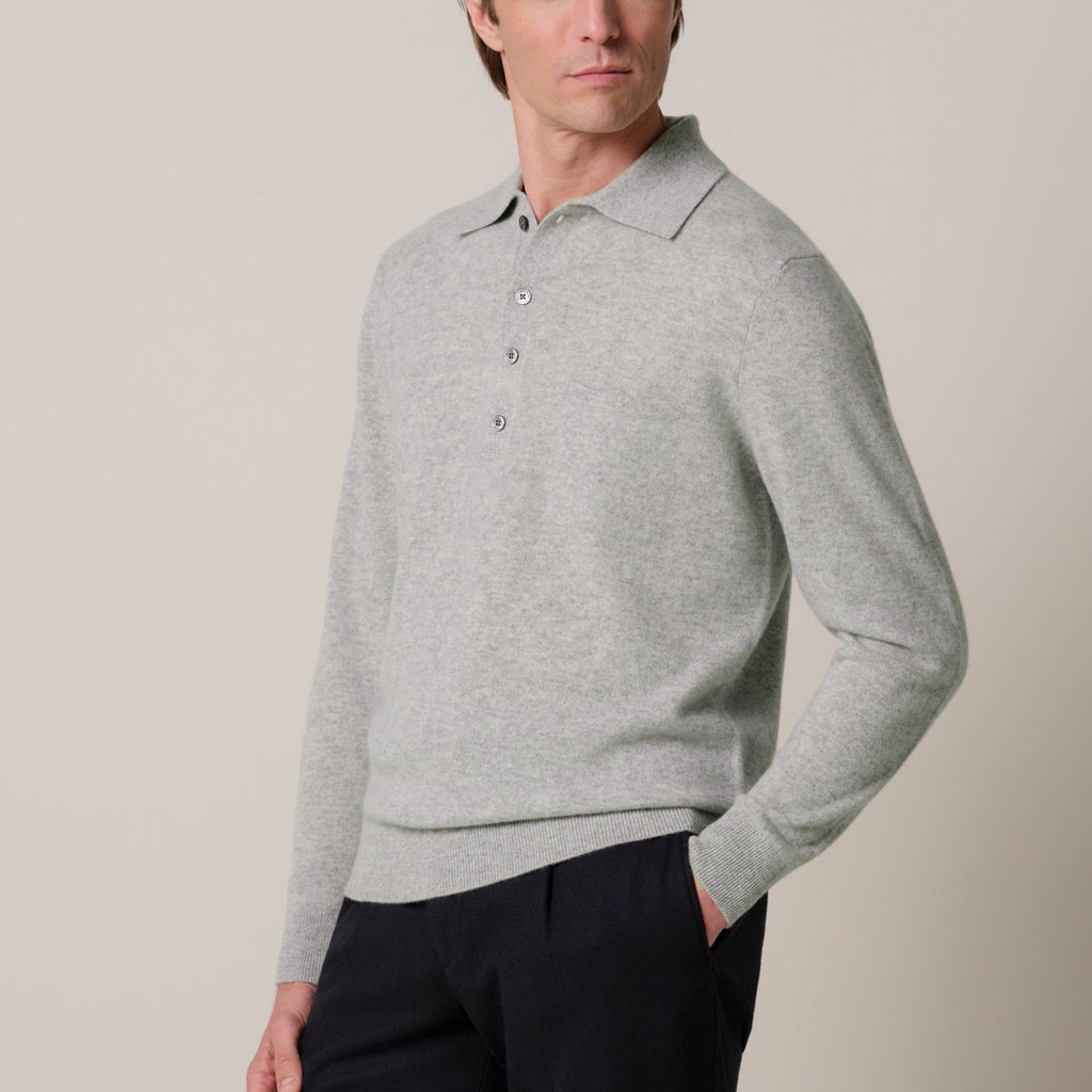 A man wearing a light gray long-sleeve knit polo sweater with a three-button placket, paired with dark trousers, photographed against a plain light beige studio background.  Profuomo Knitwear available at Sakks Menswear in Southampton.