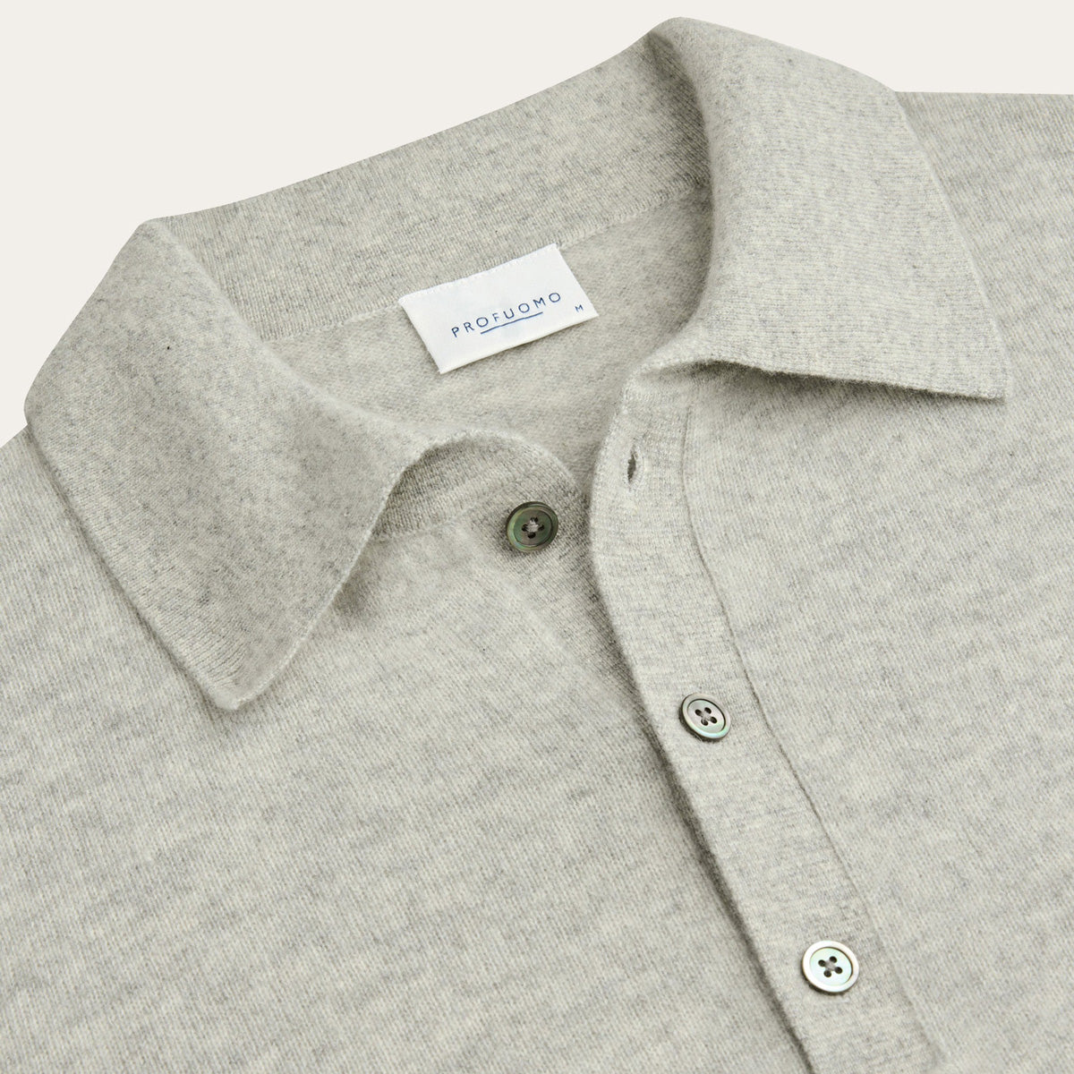 Close-up of a light heather gray knit polo shirt collar with green buttons and a visible PROFUOMO neck label. Profuomo Knitwear available at Sakks Menswear in Southampton.