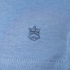Close-up of light blue fabric with a small embroidered crown logo in a darker blue-gray thread. Thomas Maine T-Shirts available at Sakks Menswear in Southampton.