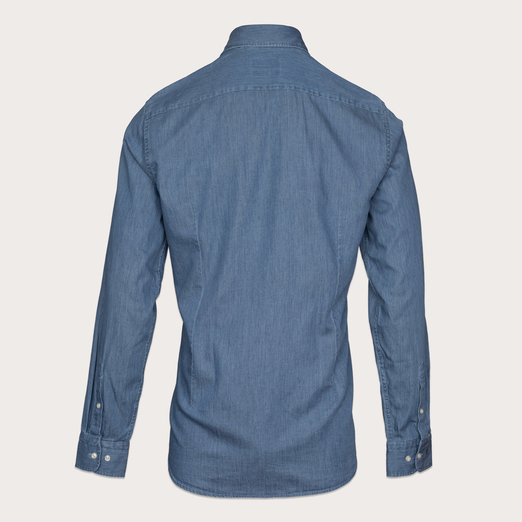 A blue denim long-sleeve button-down shirt shown from the back, displayed on a clean, solid, light beige background. Thomas Maine Shirt available at Sakks Menswear in Southampton.