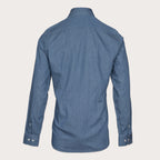 A blue denim long-sleeve button-down shirt shown from the back, displayed on a clean, solid, light beige background. Thomas Maine Shirt available at Sakks Menswear in Southampton.