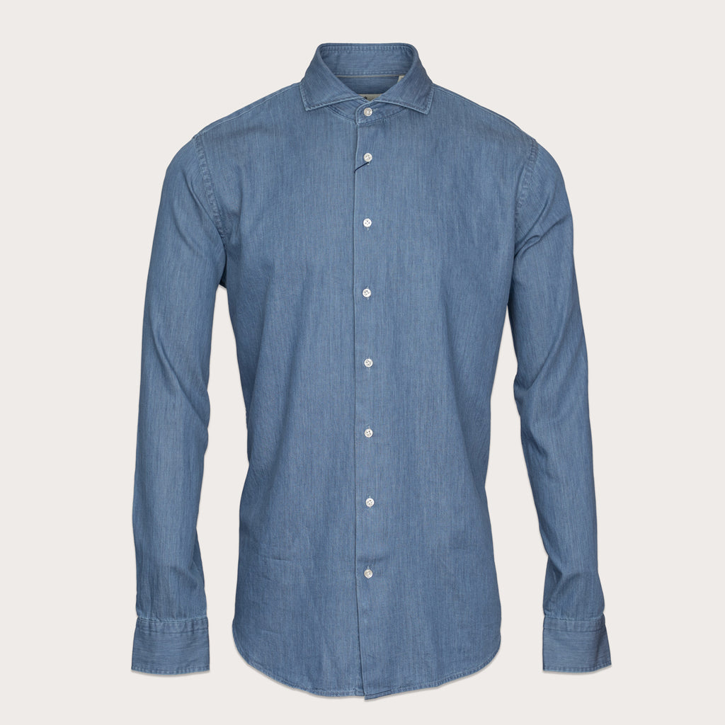 A medium blue chambray long-sleeve button-down shirt with a classic collar and white buttons, displayed on a neutral light beige background. Thomas Maine Shirt available at Sakks Menswear in Southampton.