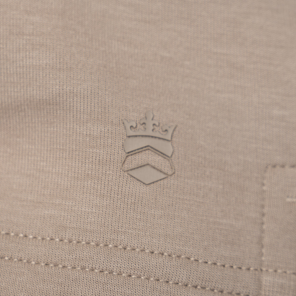 Close-up of a light beige knit fabric with a tonal embroidered crown logo centered on the chest. Thomas Maine Sweats available at Sakks Menswear in Southampton.