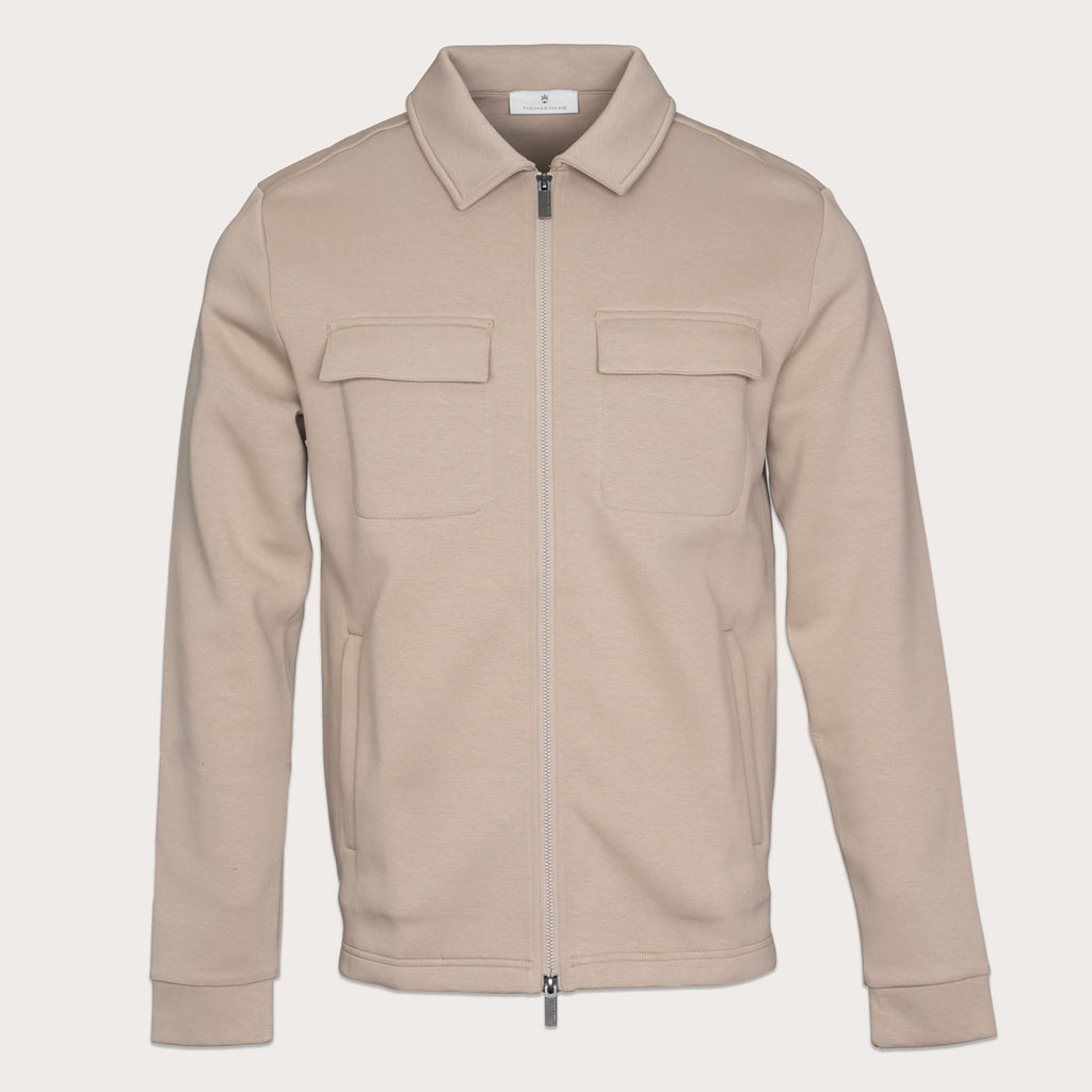 A light beige zip-up jacket with a pointed collar, two flap chest pockets, and side pockets, shown on a solid off-white background. Thomas Maine Sweats available at Sakks Menswear in Southampton.
