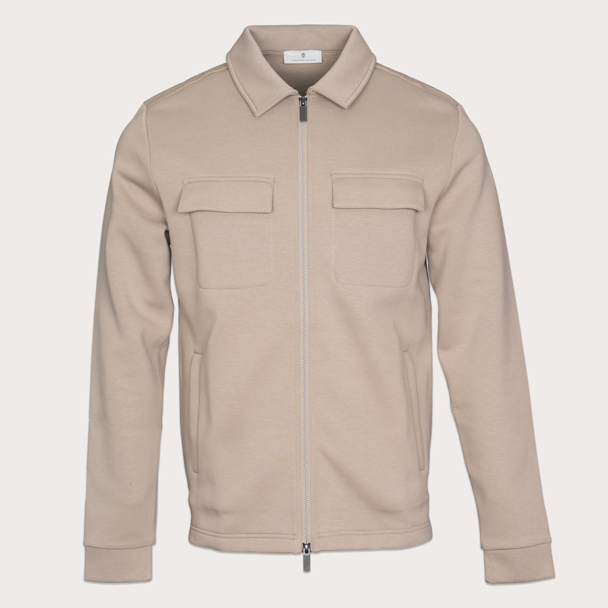 A light beige zip-up jacket with a pointed collar, two flap chest pockets, and side pockets, shown on a solid off-white background. Thomas Maine Sweats available at Sakks Menswear in Southampton.