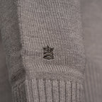 Close-up of a light gray ribbed knit garment, likely a sweater or knit accessory, featuring a small embroidered crown logo in the center. Thomas Maine Knitwear available at Sakks Menswear in Southampton.