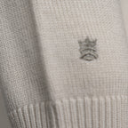 Close-up of a cream-colored knit fabric with a small embroidered gray crown logo on the side. Thomas Maine Knitwear available at Sakks Menswear in Southampton.