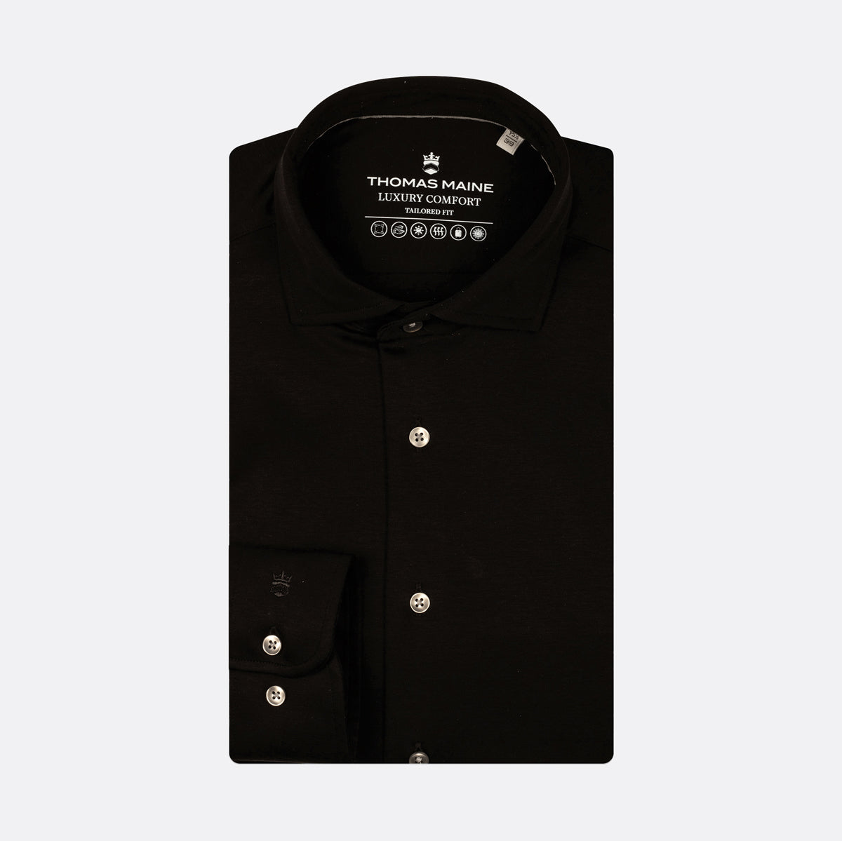 A black long-sleeve dress shirt by Thomas Maine, neatly folded to show the collar, button placket, and left chest pocket with silver buttons, set against a light gray background. Thomas Maine Shirts available at Sakks Menswear in Southampton.