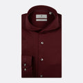 A folded burgundy long-sleeve dress shirt by Thomas Maine, featuring a pointed collar, silver buttons, and a single cuff with two buttons, displayed on a light gray background. Thomas Maine Shirts available at Sakks Menswear in Southampton.