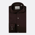A dark brown long-sleeve dress shirt by Thomas Maine, neatly folded to show the collar, button-down front, and a single-button cuff, set against a light gray background. Thomas Maine Shirts are available at Sakks Menswear in Southampton.