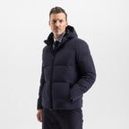 Model wearing the UBR Bolt down Jacket in Navy. Model is wearing the puffer coat with a pair of smart navy trousers. The model is stood in front of a light grey background. UBR Jackets available at Sakks Menswear in Southampton.