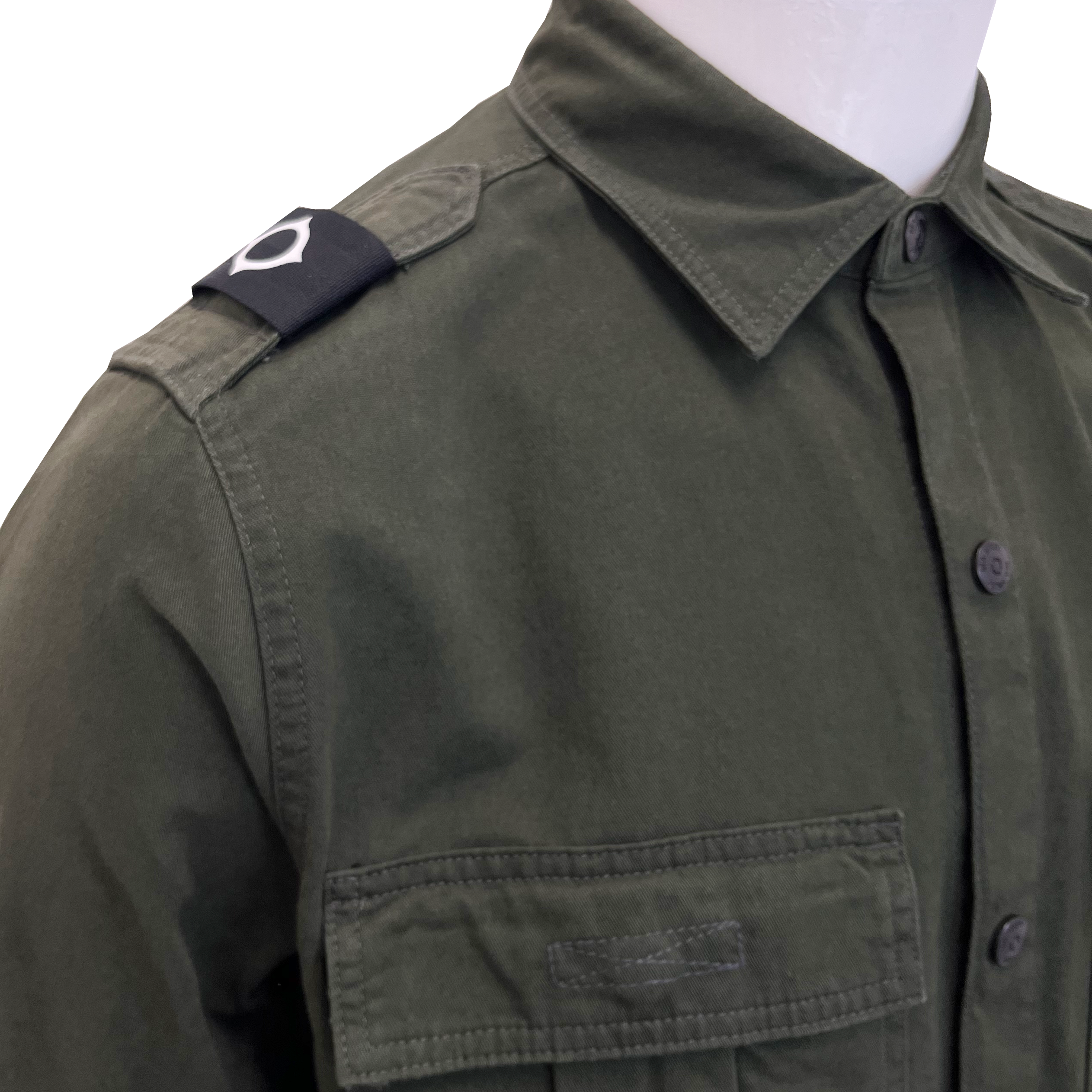 An olive green military-style shirt jacket displayed on a white mannequin torso, featuring a pointed collar, dark buttons, a chest pocket, and a black shoulder tab with a white insignia. MA.Strum Shirt Jacket available at Sakks Menswear in Southampton.
