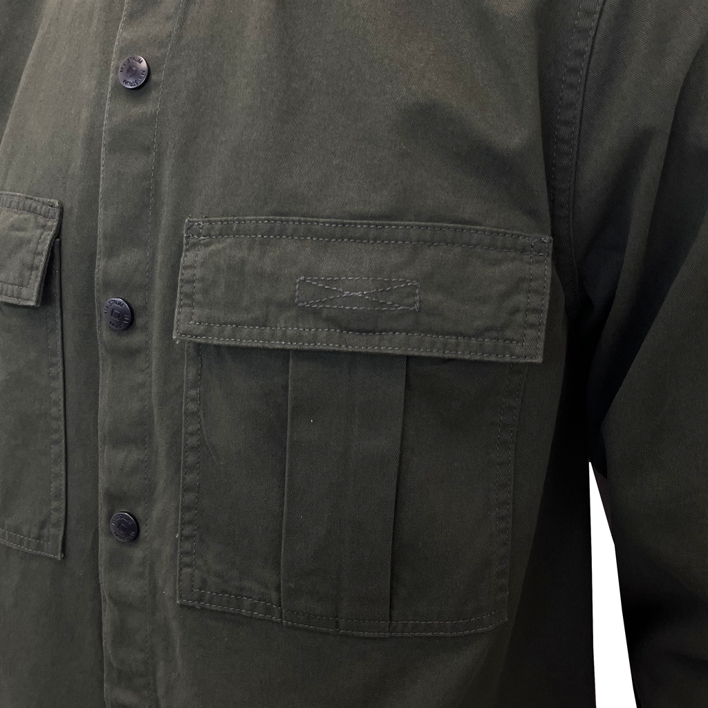 Close-up of an olive green utility jacket with a buttoned front and a large chest pocket. MA.Strum Shirt Jacket available at Sakks Menswear in Southampton.