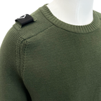 Close-up of an olive green ribbed knit sweater on a white mannequin torso, showing a black shoulder patch with a white stylised logo. MA.Strum Jumper available at Sakks Menswear in Southampton.