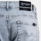 Close-up of the back waistband and pocket area of light-wash denim jeans, showing a black size label reading 32 slimmy tapered and a small brand patch on the pocket. 7 For All Mankind Jeans available at Sakks Menswear in Southampton.