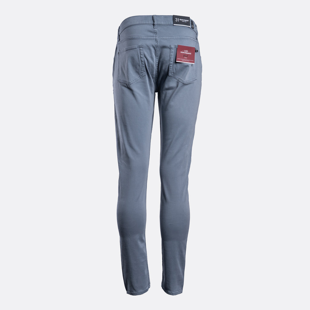 A pair of slim-fit blue jeans shown from the back, featuring a dark waistband patch and a red brand label on the right pocket, set against a plain light gray background. 7 For All Mankind Chinos available at Sakks Menswear in Southampton.