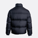 A dark navy blue puffer jacket shown from the back, featuring horizontal quilting and a high collar, set against a plain light gray background. Emporio Armani Down Jacket. Sakks Menswear Southampton.