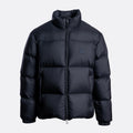 A black puffer jacket with horizontal quilting, a high stand-up collar, and a small tonal square logo patch on the left chest, shown against a light gray background. Emporio Armani Down Jacket. Sakks Menswear Southampton.