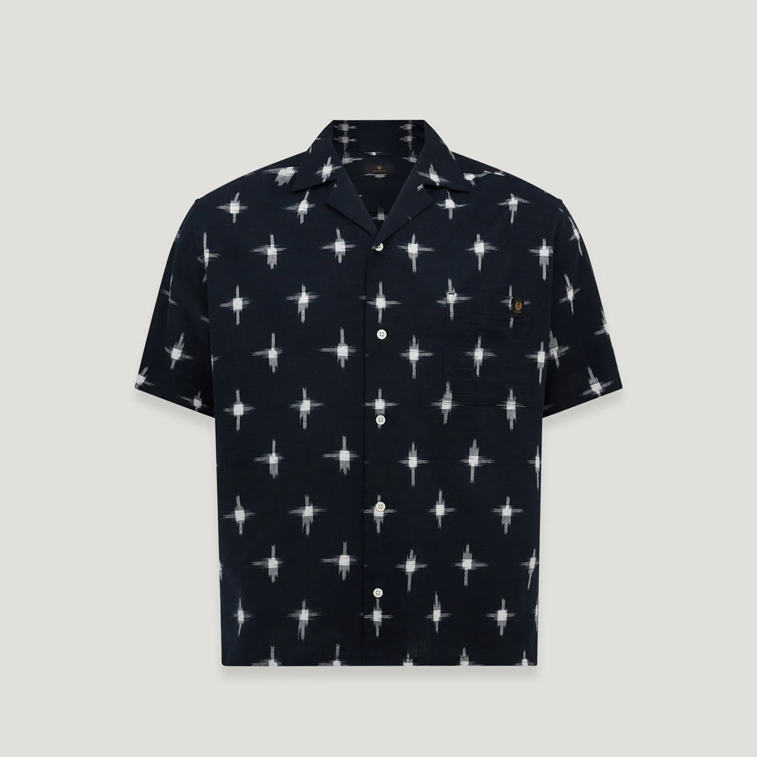 A short-sleeve button-up camp shirt in navy blue with a repeating white starburst pattern and a small embroidered logo on the chest pocket, shown against a light gray background. Belstaff Short Sleeve Shirt. Sakks Menswear Southampton.