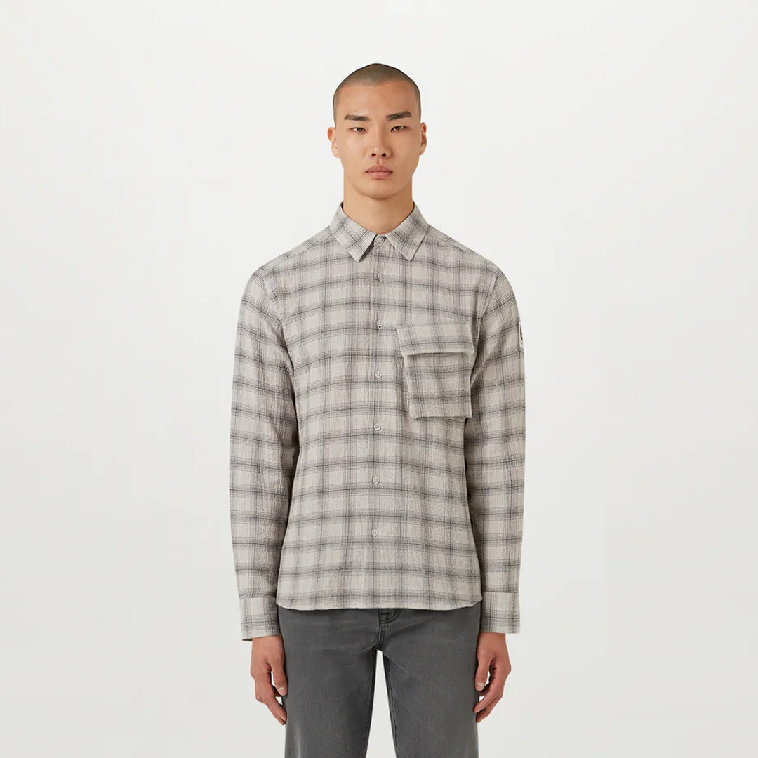 A man wearing a light gray and white plaid long-sleeve button-up shirt with a chest pocket, paired with dark gray jeans, standing against a plain white studio background. Belstaff Shirt. Sakks Menswear Southampton.