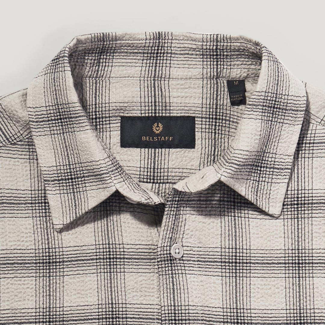Close-up of a Belstaff plaid shirt collar and upper chest in a textured fabric, featuring a black neck label with gold lettering. Belstaff Shirt. Sakks Menswear Southampton.