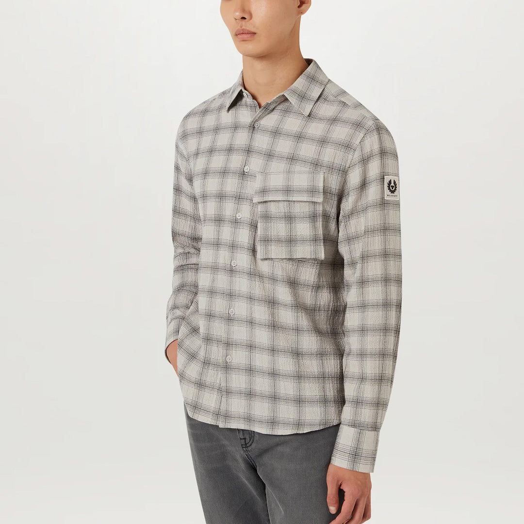 A man wearing a long-sleeve plaid button-up shirt in gray and white, paired with gray jeans, photographed against a clean white studio background. Belstaff Shirt. Sakks Menswear Southampton.