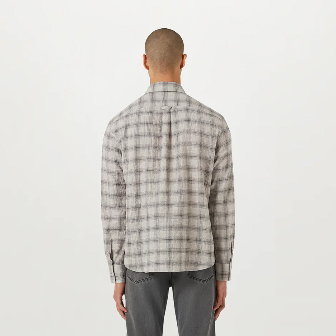 A man viewed from behind wearing a light beige and gray plaid long-sleeve shirt and gray trousers, standing against a plain white studio background. Belstaff Shirt. Sakks Menswear Southampton.