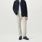 A model wearing a dark navy corduroy jacket over a white t-shirt, paired with beige straight-leg chinos and navy lace-up shoes, shot against a light gray studio background. Belstaff Chino available at Sakks Menswear in Southampton.