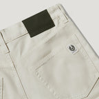 Close-up of the back waistband and pocket area of light beige denim jeans, showing a dark olive brand patch at the back waist and a small white embroidered Paddyus logo patch on the pocket. Belstaff Chino available at Sakks Menswear in Southampton.