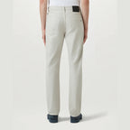 A person shown from the back wearing light beige straight-leg jeans, a white top, and dark blue shoes against a light gray studio background. Belstaff Chino available at Sakks Menswear in Southampton.