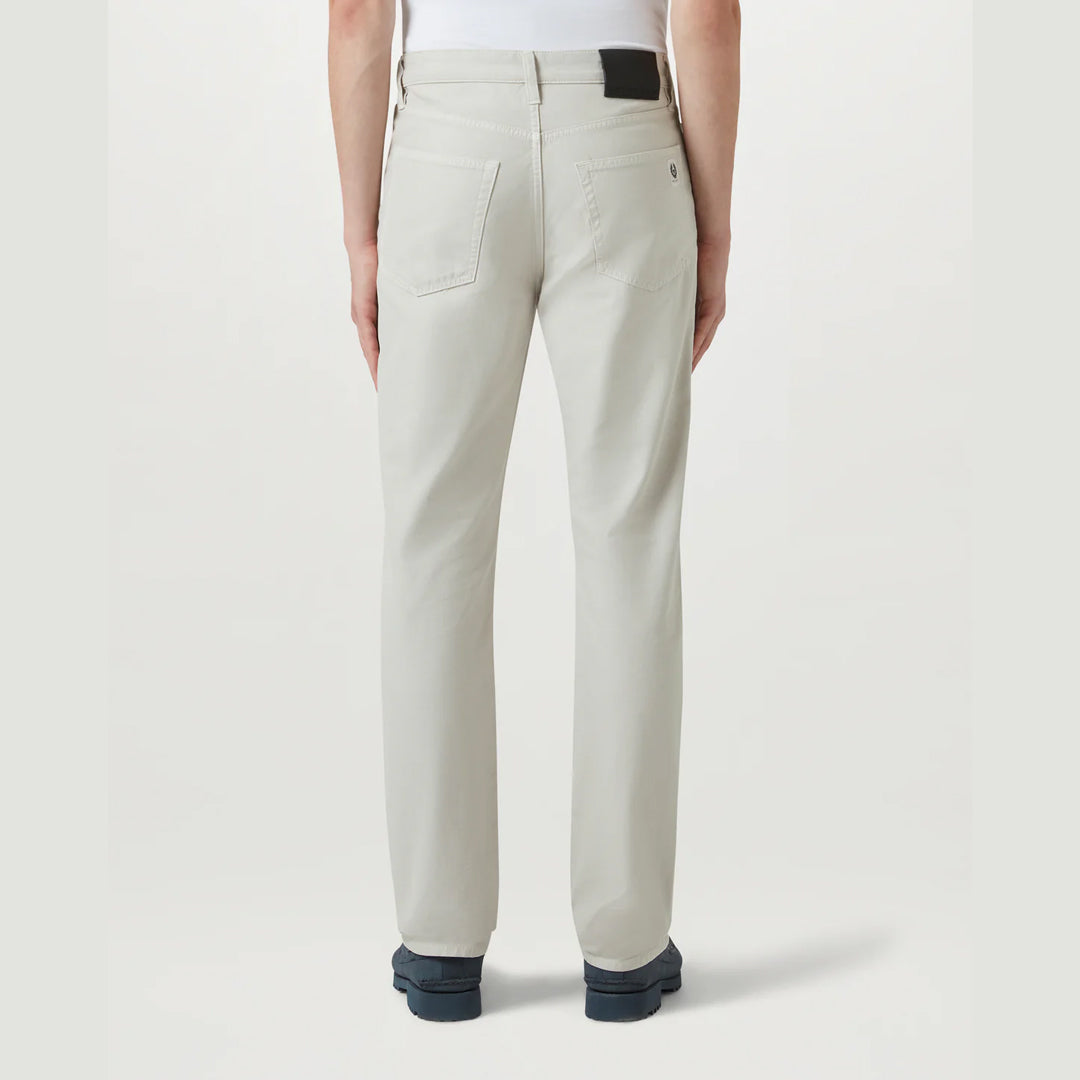 A person shown from the back wearing light beige straight-leg jeans, a white top, and dark blue shoes against a light gray studio background. Belstaff Chino available at Sakks Menswear in Southampton.