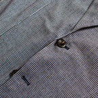 Close-up of a textured woven fabric with a fine micro-check pattern in gray, white, and subtle blue tones, featuring a dark metal button and a small dark accent. Circolo 1901 Blazer available at Sakks Menswear in Southampton.