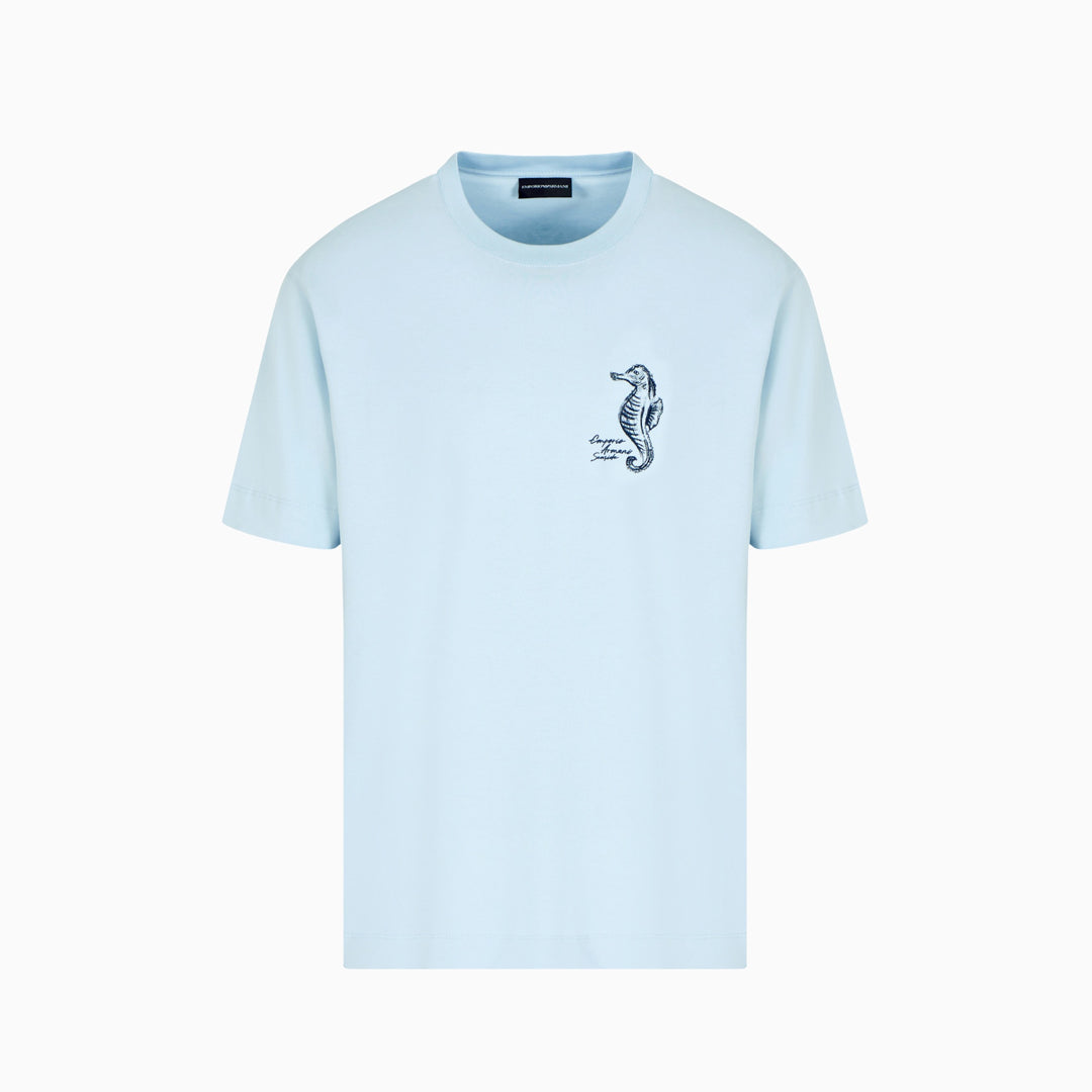 A light blue short-sleeve crewneck t-shirt with a small black seahorse graphic on the left chest, displayed on a clean white background. Emporio Armani T-Shirt. Sakks Menswear Southampton.